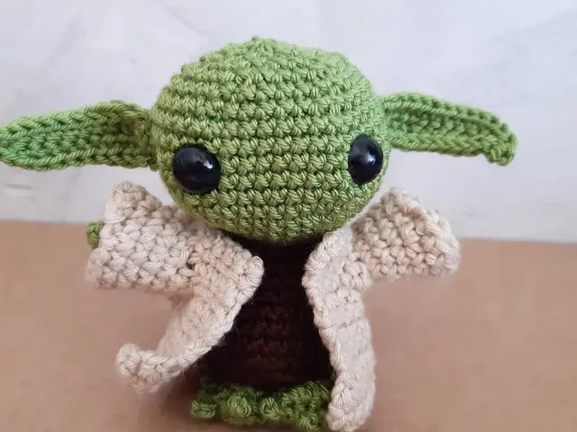 Amigurumi de un pequeño alienígena verde con orejas grandes y túnica beige, tejido a crochet