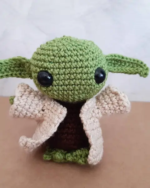 Amigurumi de un pequeño alienígena verde con orejas grandes y túnica beige, tejido a crochet
