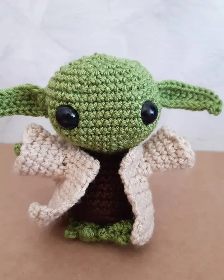 Amigurumi de un pequeño alienígena verde con orejas grandes y túnica beige, tejido a crochet