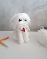 Amigurumi de bichón maltés blanco con lazo azul, tejido a crochet, junto a un ovillo y una aguja