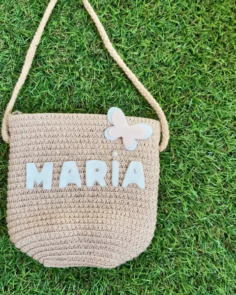 Bolsito de paja para niña con el nombre María y una mariposa de fieltro blanco, sobre césped