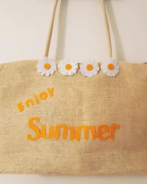 Bolso de paja natural con la palabra Summer y margaritas de fieltro amarillo, sobre césped