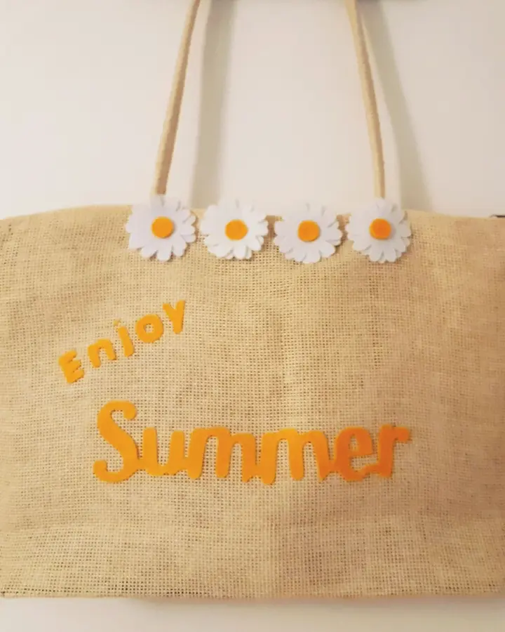 Bolso de paja natural con la palabra Summer y margaritas de fieltro amarillo, sobre césped