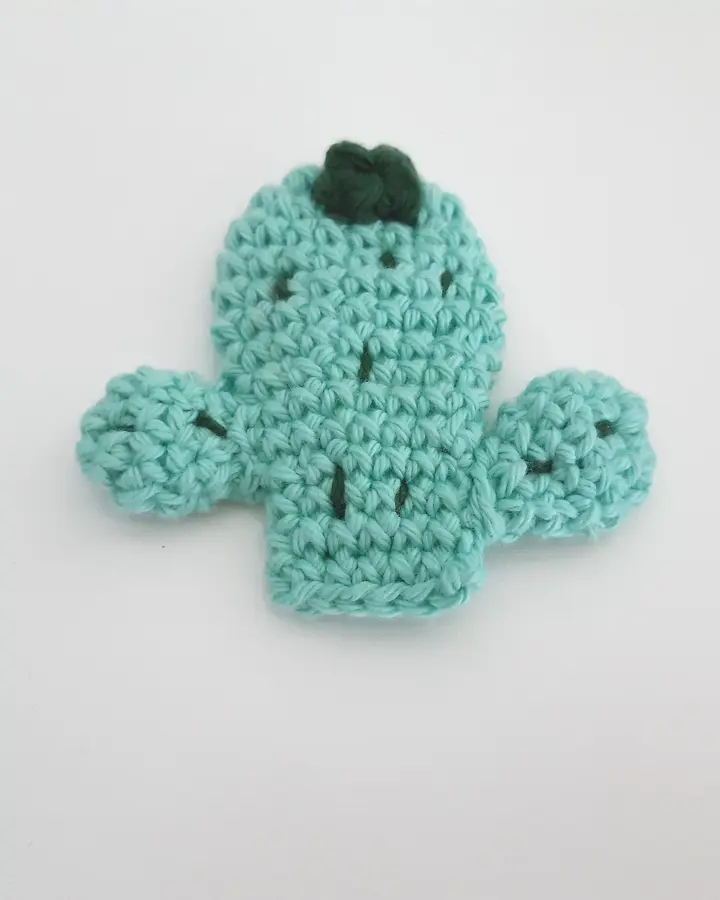 Broche de crochet con forma de cactus verde en maceta, con una flor, sobre fondo claro