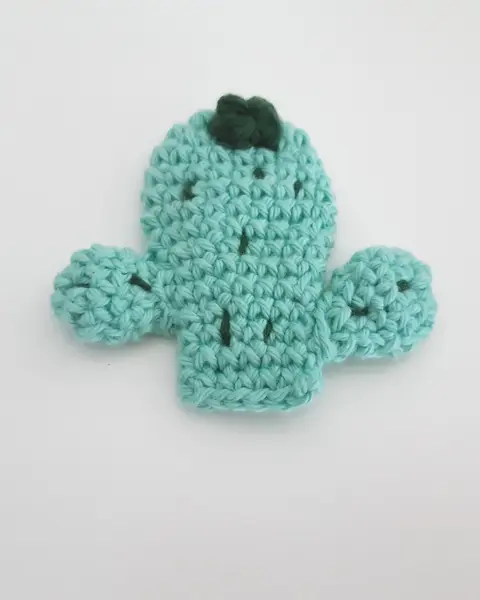 Broche de crochet con forma de cactus verde en maceta, con una flor, sobre fondo claro