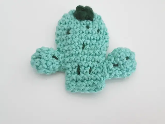 Broche de crochet con forma de cactus verde en maceta, con una flor, sobre fondo claro