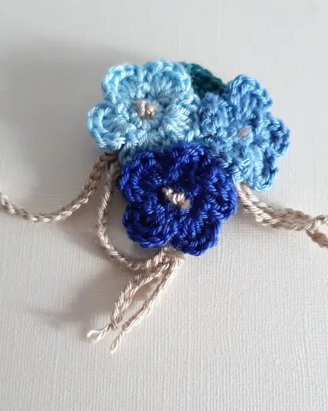 Broche de crochet con un ramillete de flores azules y blancas con botones en el centro