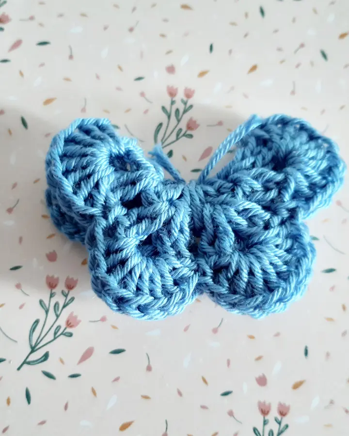 Broche de crochet con forma de mariposa en dos tonos de azul sobre papel de flores