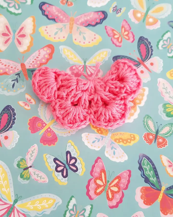 Broche de crochet con forma de mariposa fucsia con bordes blancos sobre papel de flores