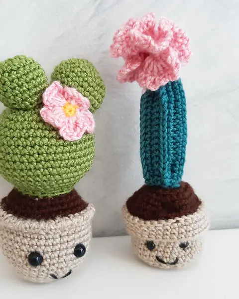 Dos cactus de crochet verdes con flor rosa y maceta tejida, sobre fondo blanco