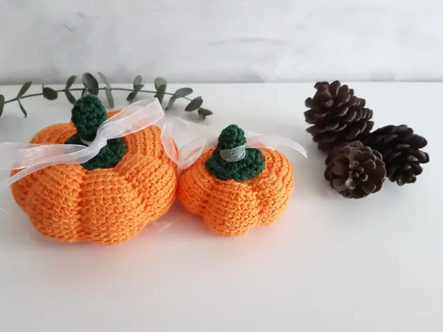 Tres calabazas de crochet naranjas de distinto tamaño con rabito verde, junto a piñas