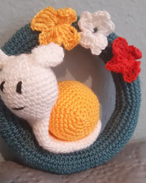 Caracol de amigurumi con concha verde decorada con flores de colores, tejido a crochet