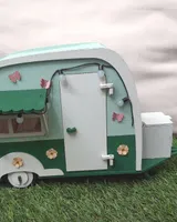 Maqueta de caravana de madera pintada en verde y crema, con toldo y ventanas, sobre césped