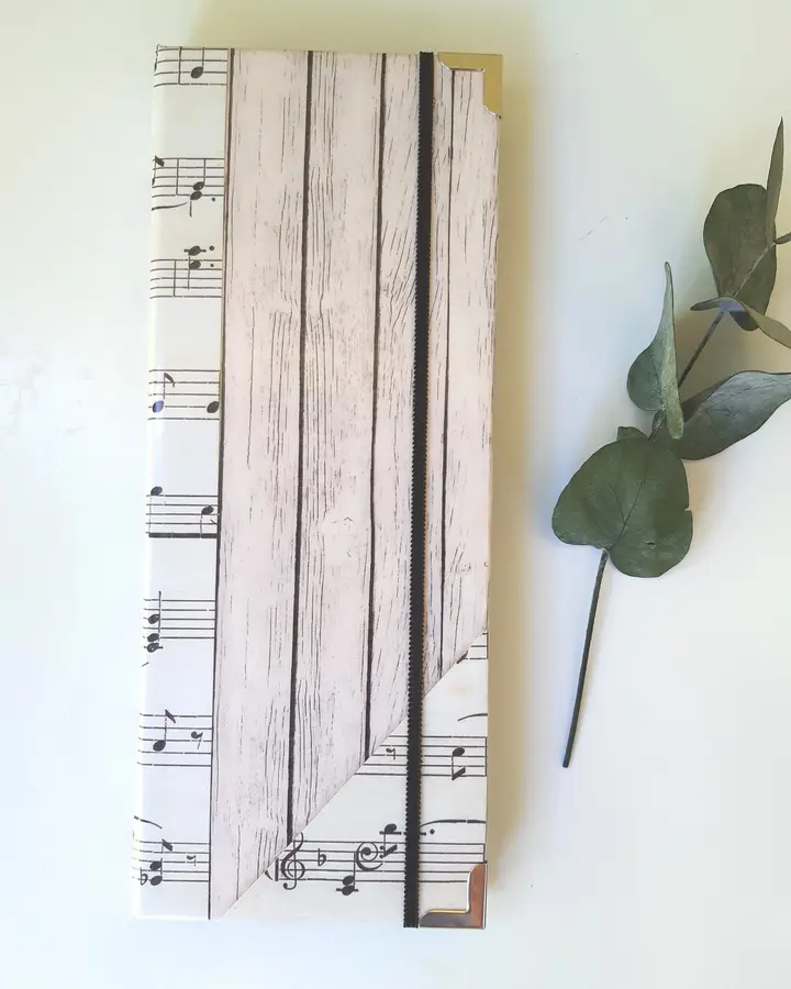 Porta tratados forrado con papel de partituras en tonos crema y sepia, con cierre de goma