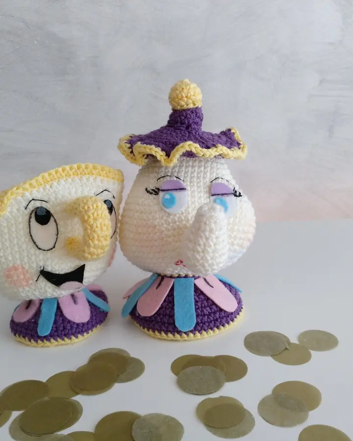 Amigurumis de una tetera blanca con tapa lila y una tacita con cara sonriente, tejidos a crochet