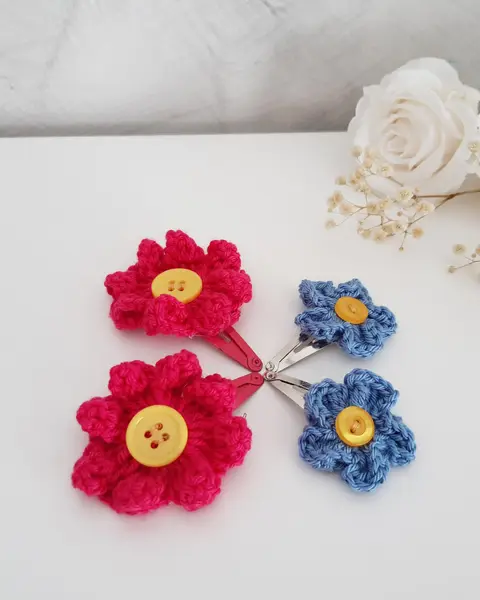 Dos clips de pelo con flores de crochet en rojo, amarillo y azul, con botones en el centro