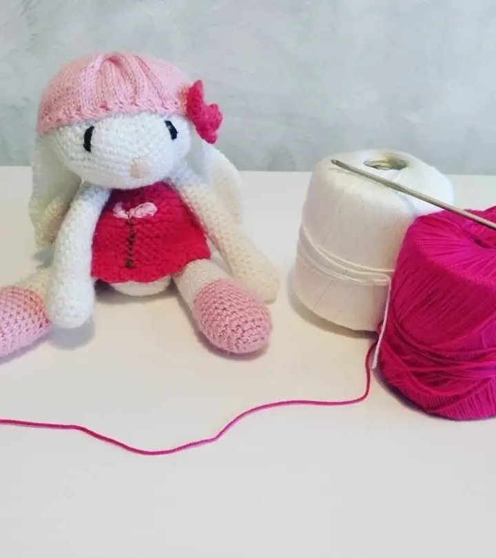 Amigurumi de una conejita con vestido rosa y lazo, tejida a crochet, sentada sobre fondo claro