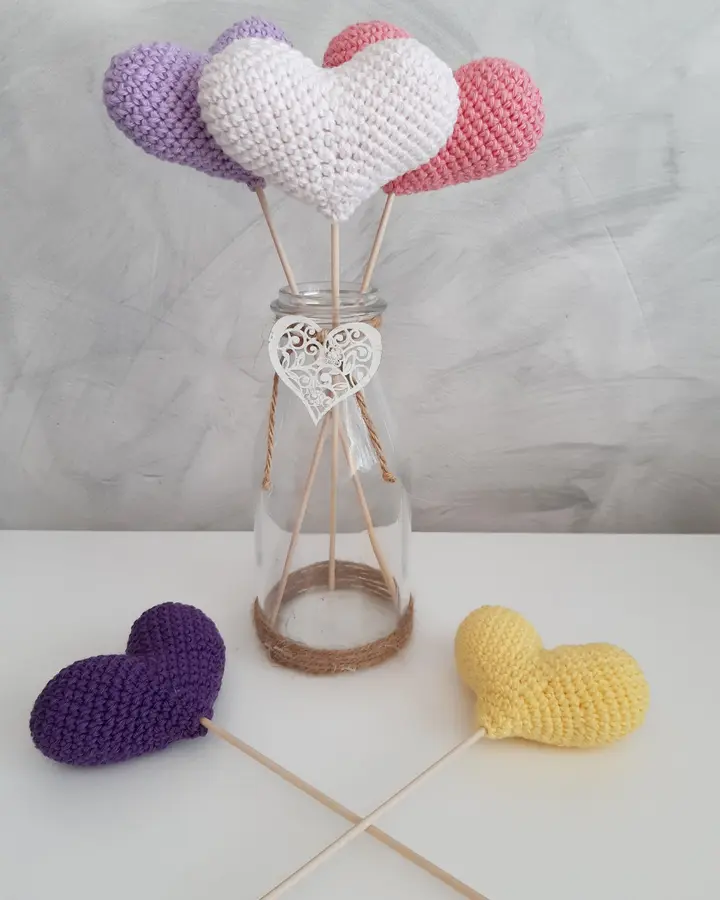Corazones de crochet en rosa, amarillo y turquesa montados sobre varillas dentro de un jarrón