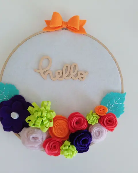 Bastidor de madera con flores de fieltro de colores y la palabra Hello en madera en el centro