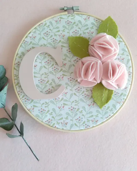 Bastidor de madera con una letra pintada a mano sobre tela y flores de fieltro alrededor