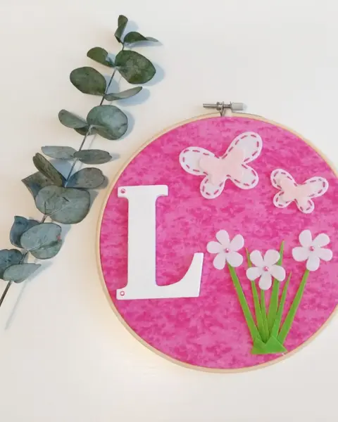 Bastidor de madera con la letra L sobre tela rosa y mariposas de fieltro en relieve