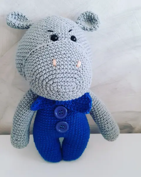 Hipopótamo amigurumi gris con peto azul y botones, tejido a crochet