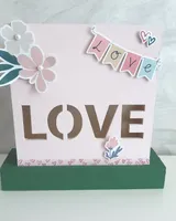 Lámpara de madera blanca con la palabra Love recortada y frente decorado con papel