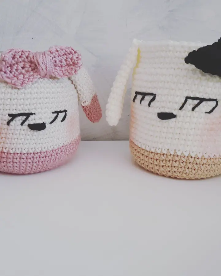 Dos lapiceros de crochet con carita bordada y lazo, de distinto tamaño, sobre una mesa