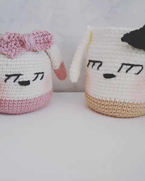 Dos lapiceros de crochet con carita bordada y lazo, de distinto tamaño, sobre una mesa