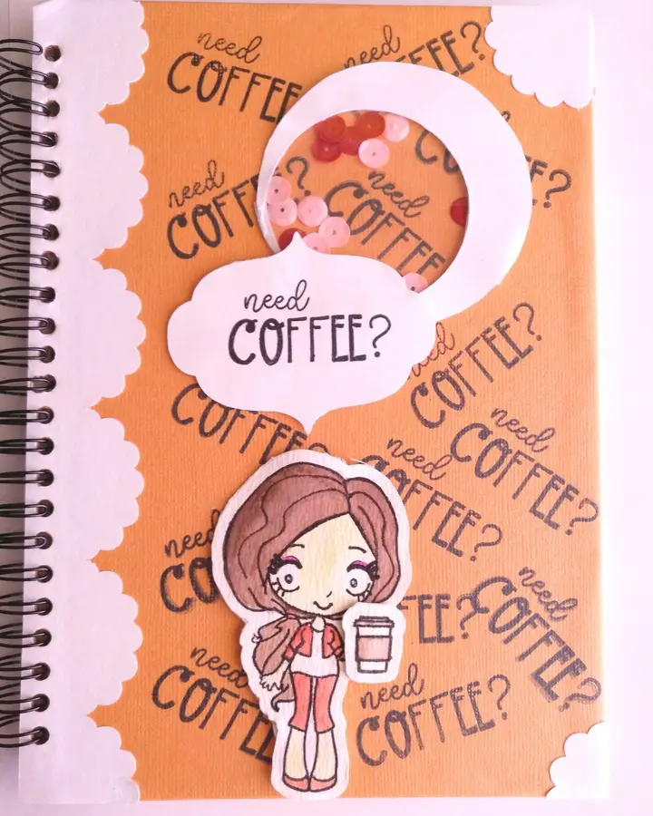 Libreta de anillas con portada naranja de café, sellos recortados a mano y una figurita con taza