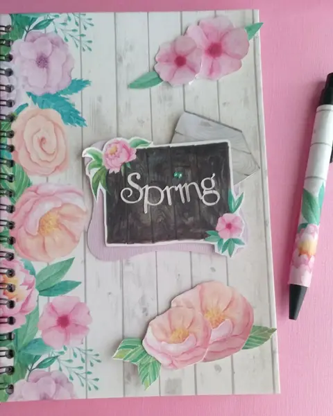 Libreta de anillas con portada Spring, flores de papel en relieve y brillantitos, junto a un bolígrafo