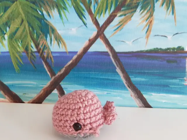Llavero de ballena azul turquesa tejida a crochet con anilla metálica, sobre fondo de playa