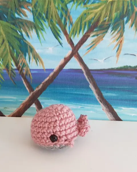 Llavero de ballena azul turquesa tejida a crochet con anilla metálica, sobre fondo de playa