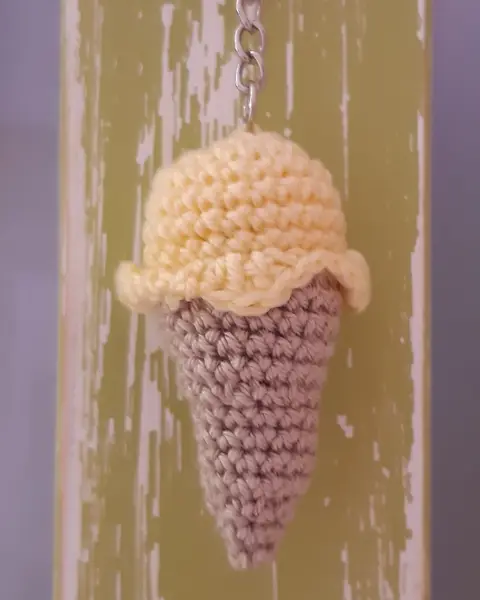 Llavero de crochet con forma de cucurucho de helado amarillo y barquillo beige sobre madera pintada