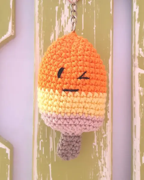 Llavero de crochet con forma de polo de helado a franjas naranja, rosa y crema con carita
