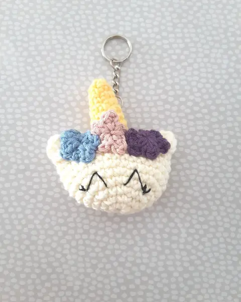 Llavero de crochet con forma de cabeza de unicornio blanca, cuerno dorado y crin lila, azul y amarilla