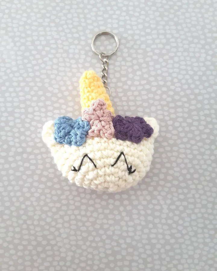 Llavero de crochet con forma de cabeza de unicornio blanca, cuerno dorado y crin lila, azul y amarilla
