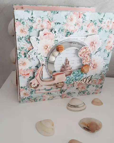 Maxi álbum de scrapbooking cerrado con tapa de flores coral y verde agua, ventana redonda y conchas