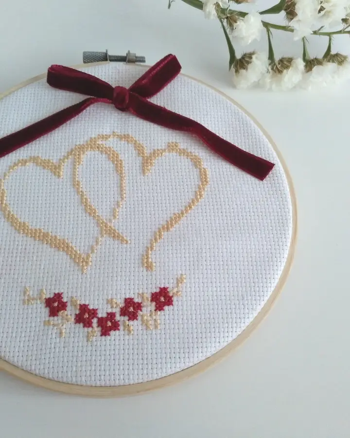 Porta alianzas en bastidor con dos corazones bordados en punto de cruz dorado y lazo granate