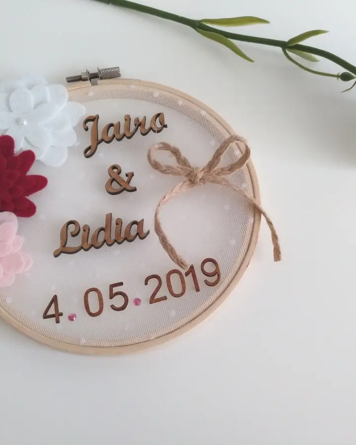 Porta alianzas en bastidor con tul rosa, flores de fieltro granate y nombres Jairo y Lidia en madera