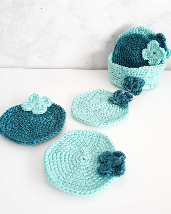 Juego de posavasos de crochet verde menta y verde botella con flores, junto a una cestita de crochet a juego