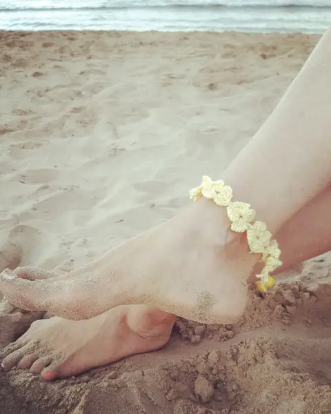 Tobillera de crochet con flores amarillas en el pie de una mujer sobre la arena de la playa