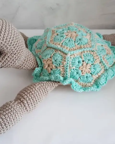 Tortuga amigurumi grande de crochet con caparazón de hexágonos verde agua y cuerpo beige, vista de lado