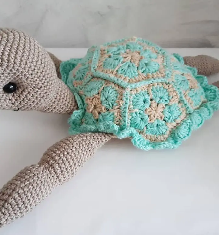 Tortuga amigurumi grande de crochet con caparazón de hexágonos verde agua y cuerpo beige, vista de lado