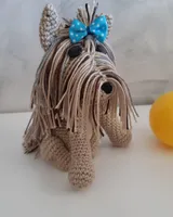 Yorkshire amigurumi de crochet con pelo largo beige y gris y lacito azul, junto a una pelota amarilla